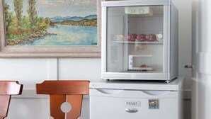 Un réfrigérateur blanc avec une porte en verre, une chaise en bois et un tableau accroché au mur.