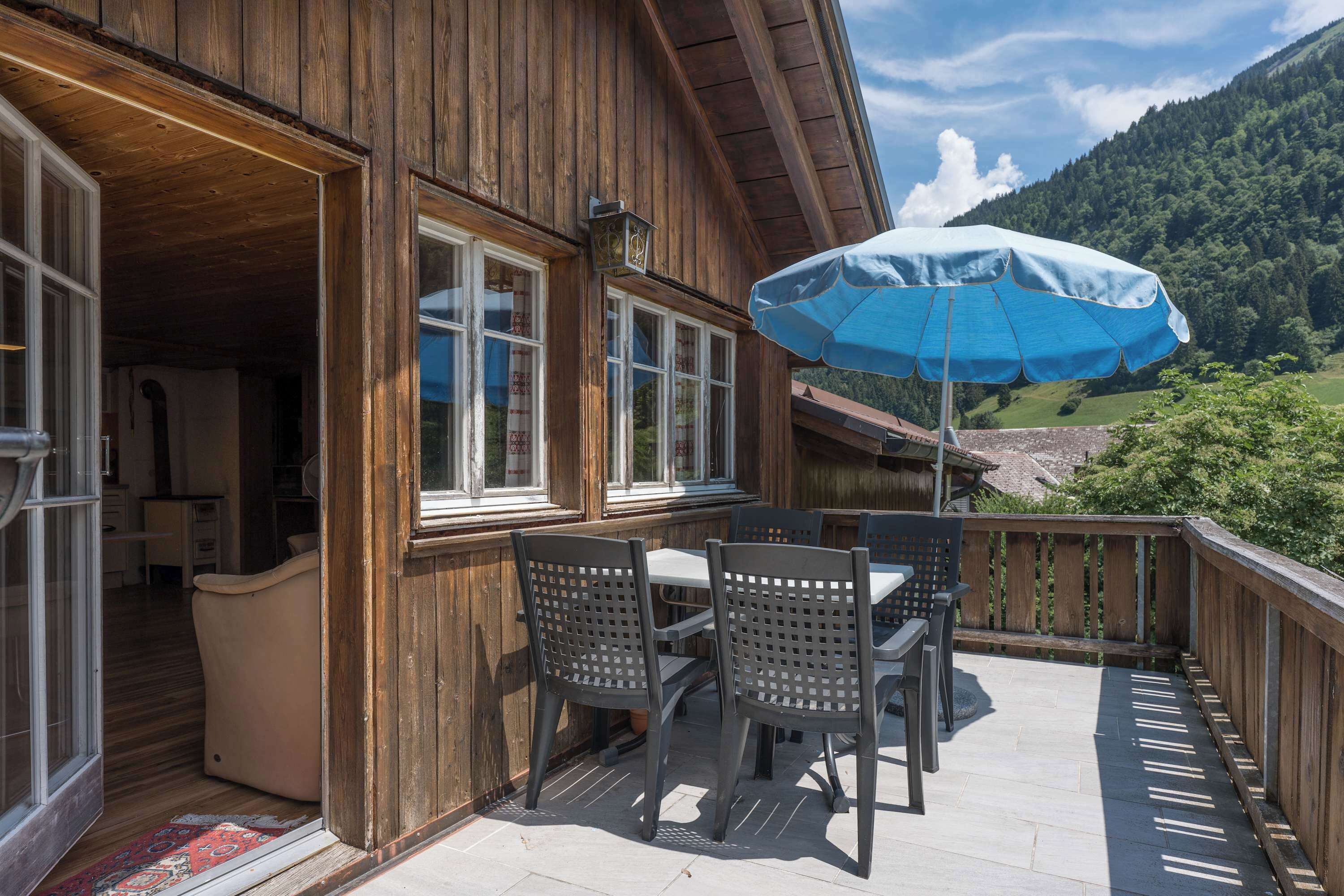 Ein hölzernes Gebäude mit Balkon, Sitzgelegenheiten im Freien und Blick auf eine gebirgige Landschaft.