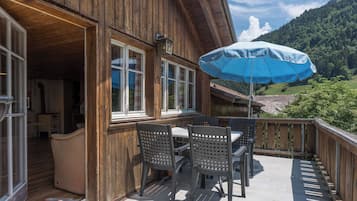 Un bâtiment en bois doté d’un balcon, d’un espace extérieur aménagé pour s’asseoir et offrant une vue sur un paysage montagneux.