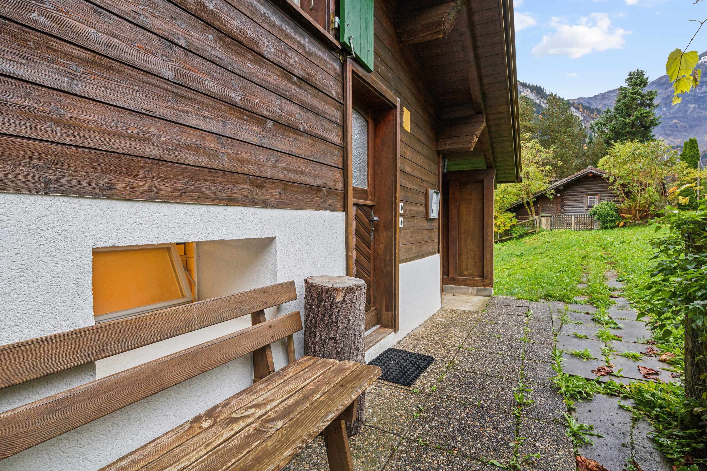 Un edificio in legno con una panchina e un tronco d'albero all'esterno, una porta e una piccola finestra.