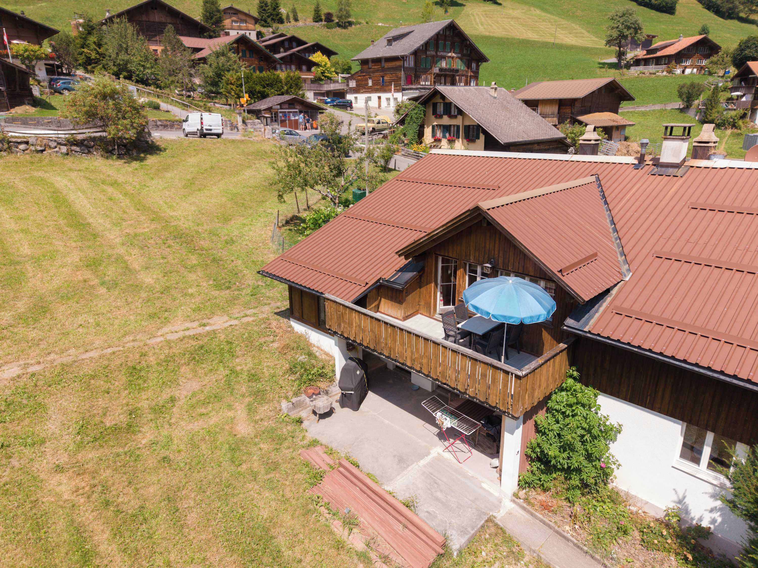 A wooden house with a balcony, a patio with outdoor furniture, and a view of a green hillside.