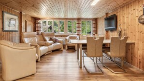 A wooden-paneled room with a sofa, chairs, a table, and a TV.