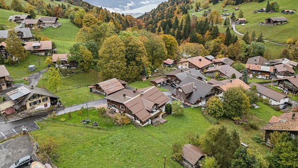 A mountainous village with traditional houses, a clear view of the valley, and a lake in the background.
