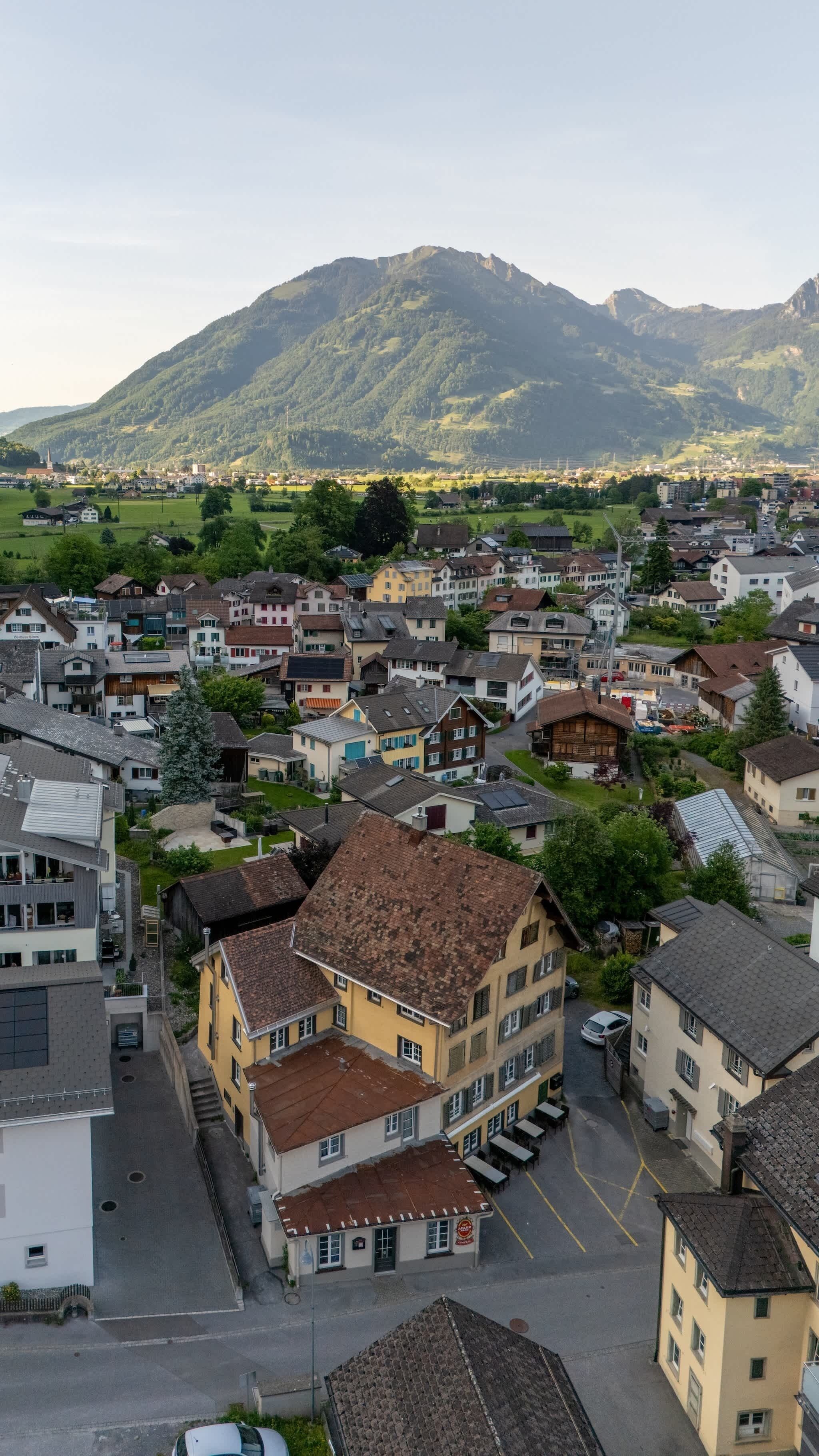 Eine Stadt mit Wohnhäusern, einem markanten gelben Gebäude mit rotem Dach und einem Berg im Hintergrund.