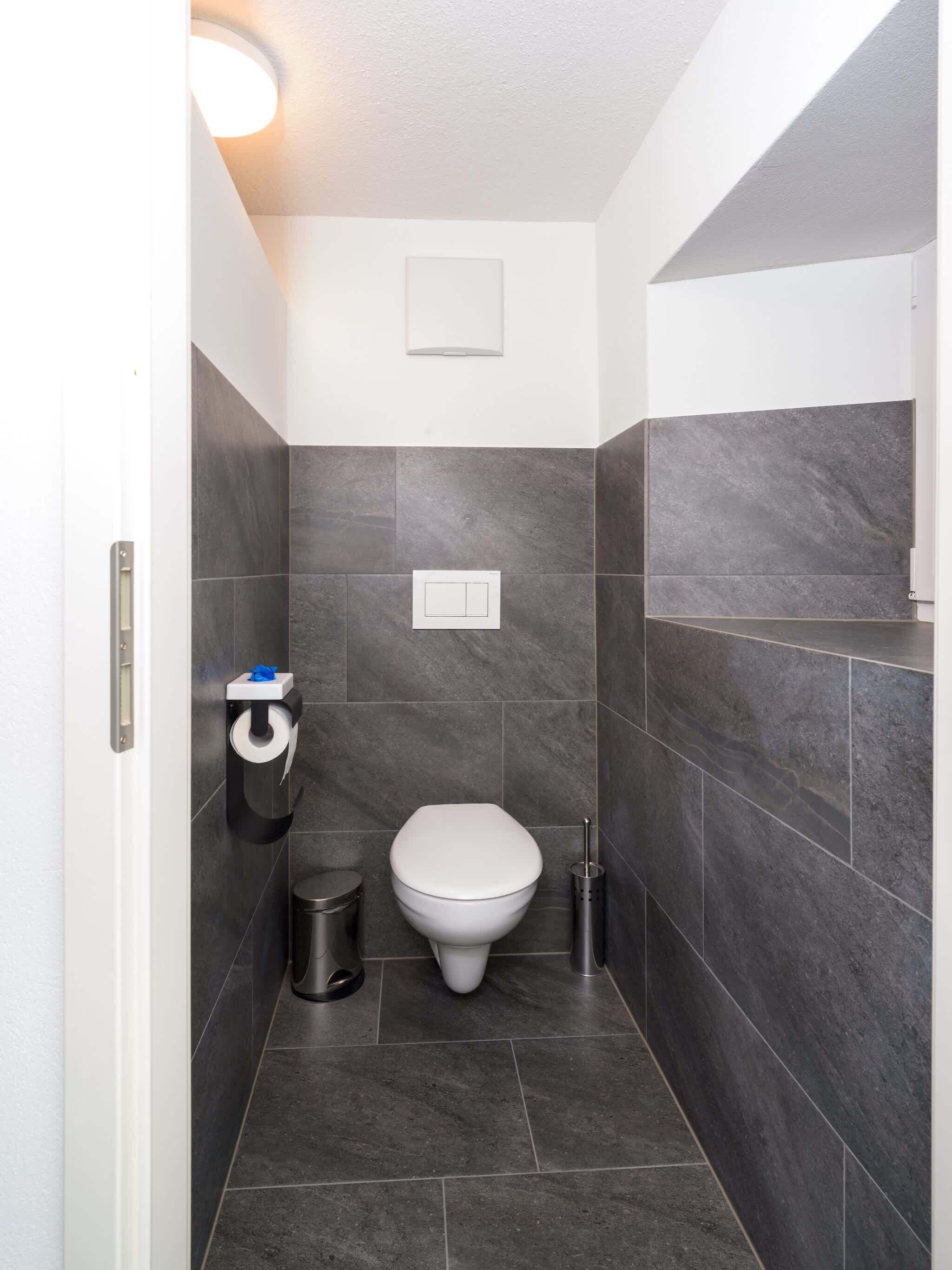 Une petite salle de bain comprenant des toilettes, une poubelle et un porte-rouleau de papier toilette.