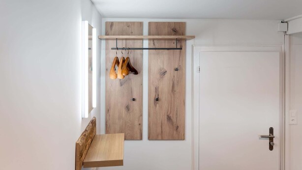 Una habitación con un banco de madera, un perchero con zapatos y una puerta.