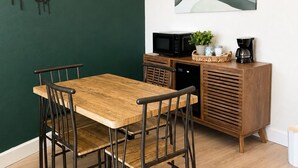 Ein Essbereich mit Holztisch und Stühlen, einer Mikrowelle, einer Kaffeemaschine und einem Schrank.