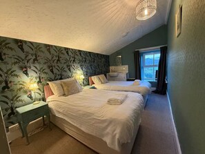 Ein Schlafzimmer mit zwei Betten, einem Nachttisch, einer Lampe, einem Fenster mit Blick und einem Kronleuchter.