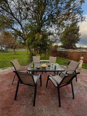 An outdoor patio with a glass table surrounded by chairs, a bowl of chips, and bottles of beer. - Monkey Gully Retreat 2 minutes from town and 45 mins from Mount buller (Mansfield)