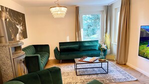 Una sala de estar moderna con un sofá verde, una mesa de centro, una chimenea y un ventanal con vistas a árboles.