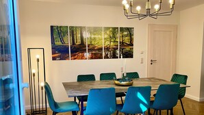 Un comedor con una mesa de madera, seis sillas, una araña y decoración de pared con motivos forestales.