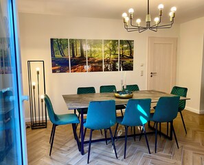 Ein Essbereich mit einem Holztisch, sechs Stühlen, einer Kristallleuchtre und Wandbildern mit Waldmotiven.