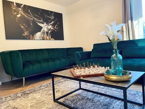 Ein modernes Wohnzimmer mit einem grünen Sofa, einem Schachbrett und einer Vase mit Blumen.