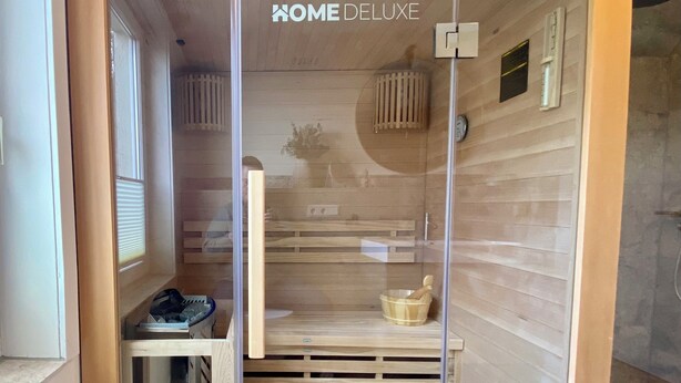 Una sauna con interior de madera, una puerta de cristal y el texto 'HOME DELUXE' en la puerta.