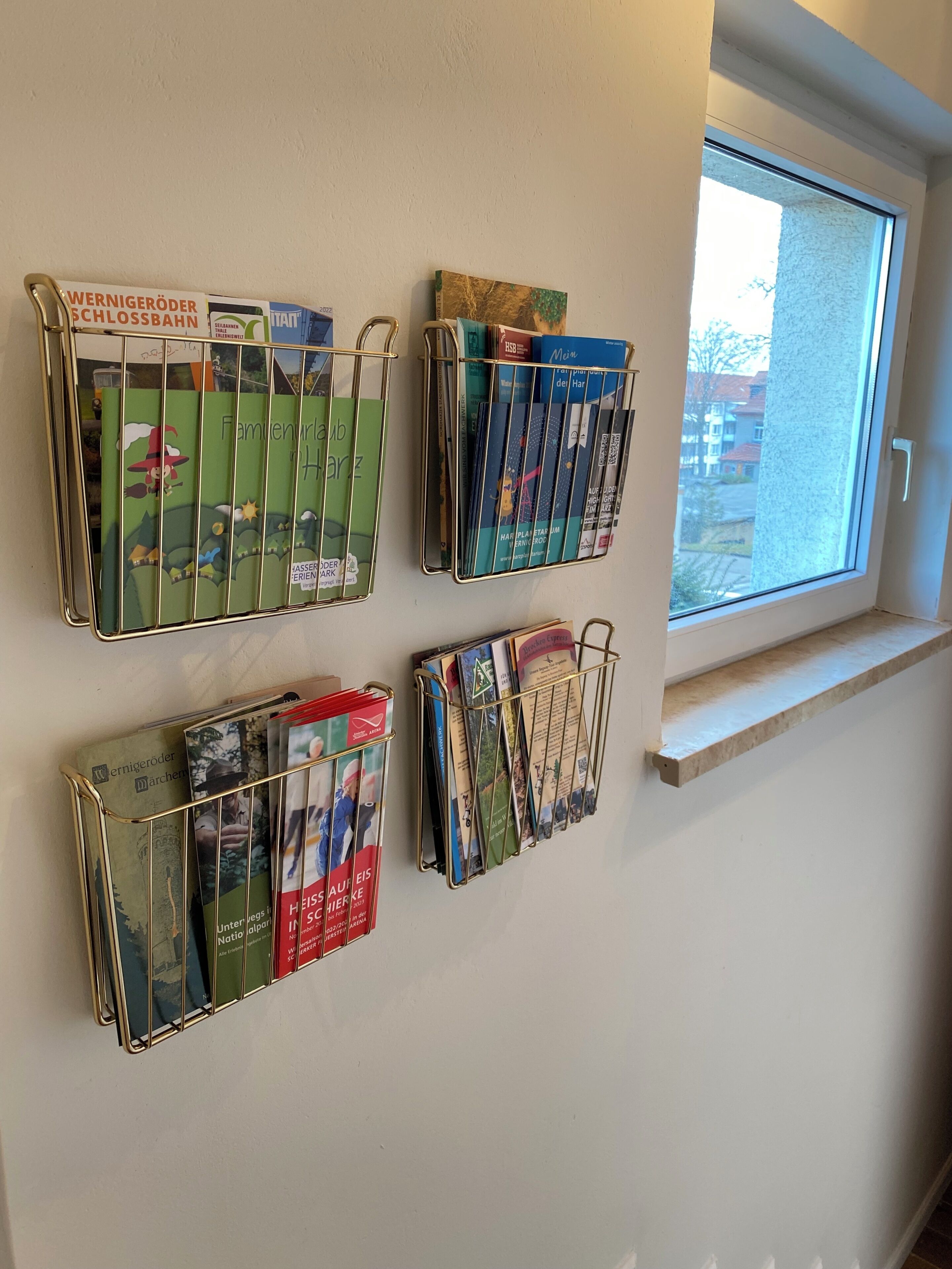 A wall with four metal book racks holding various magazines and books.
