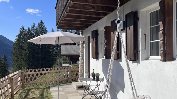 Un edificio in legno con facciata bianca, una sedia a dondolo e un tavolo con una bottiglia.