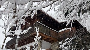 Un rifugio rustico con una veranda in legno, pareti in pietra e rami imbiancati dalla neve.