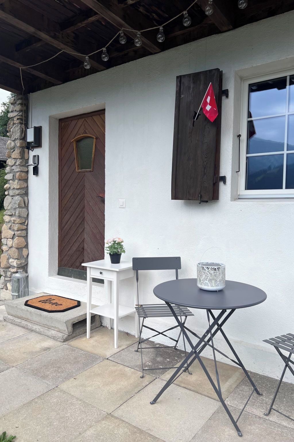 Eine Terrasse mit Tisch und Stühlen, eine Tür mit Fenster sowie eine Steinmauer.