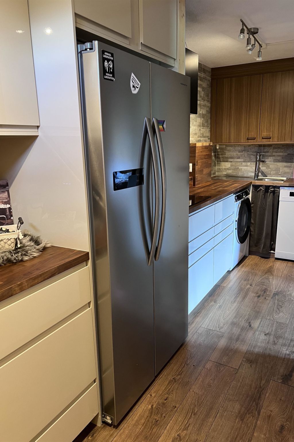 Une cuisine moderne équipée d’un réfrigérateur en acier inoxydable, de meubles de rangement en bois, d’un lave-linge et d’un lave-vaisselle.