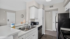 Una cocina moderna con armarios blancos, lavavajillas, cafetera y refrigerador.