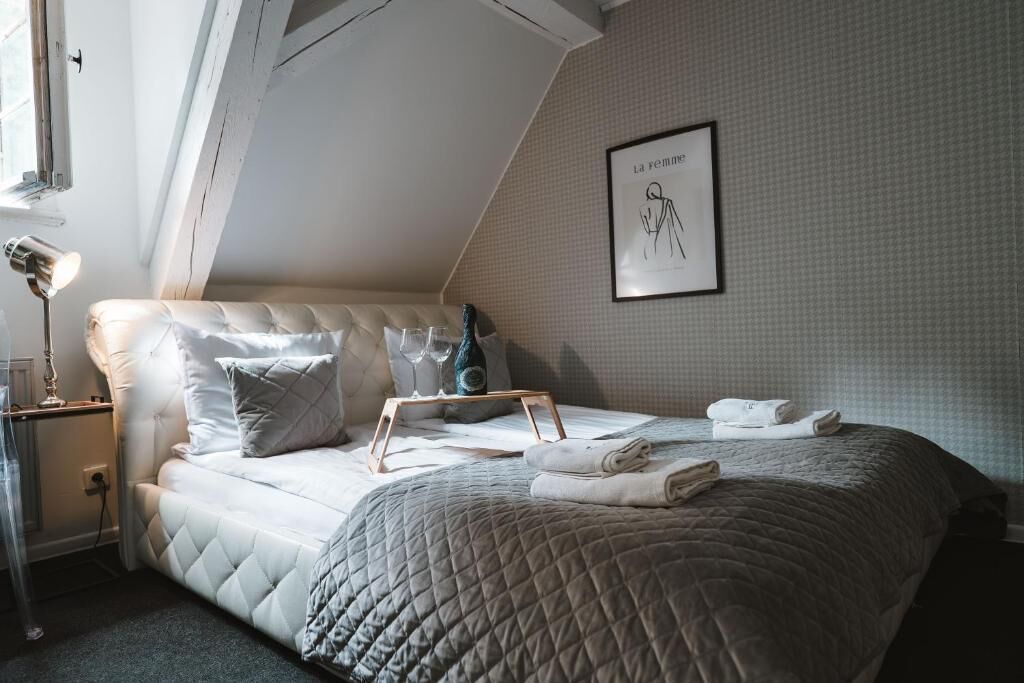 A bedroom with a bed, pillows, a bedside table with a lamp, a framed artwork on the wall, and a window.