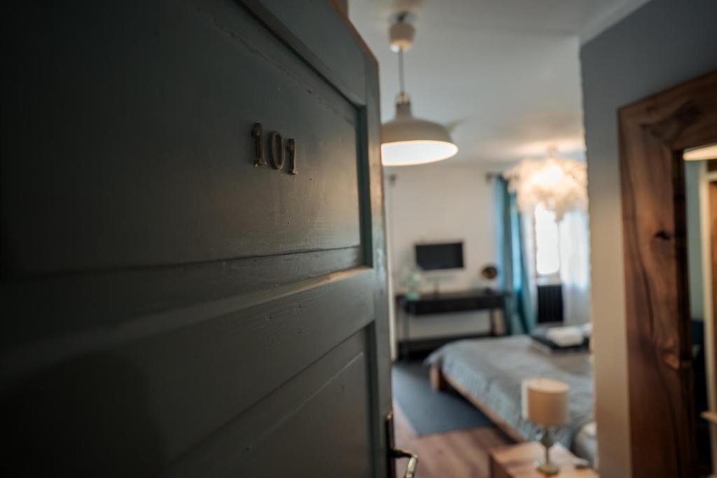 Een kamer met een bed, nachtkastje, lamp en raam met gordijnen.