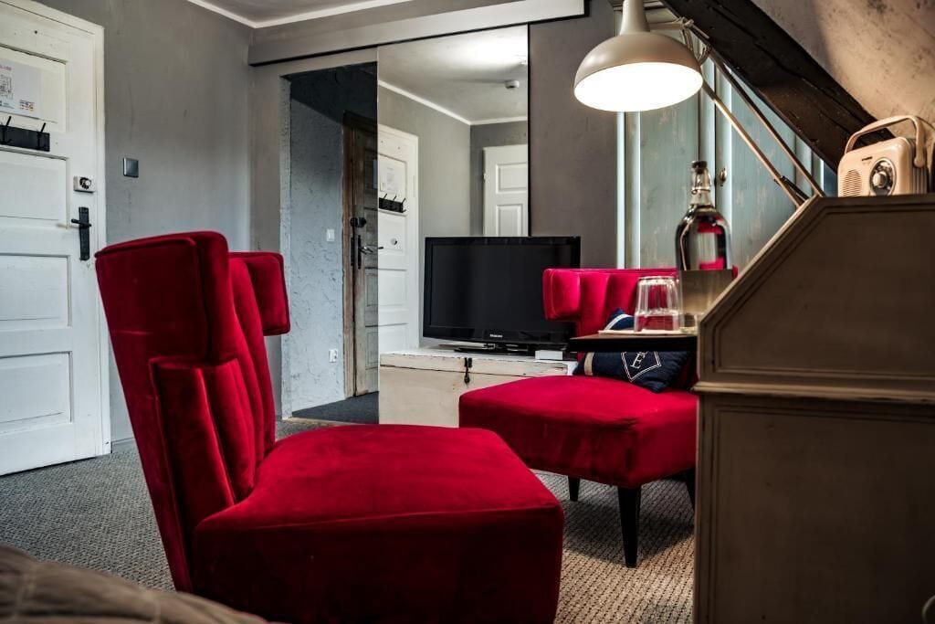 A room with a red chair, a television, and a mirror.
