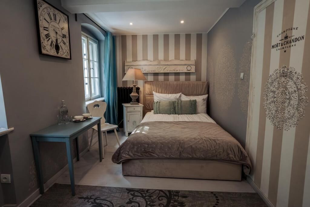Un dormitorio con cama, escritorio, silla, ventana y un reloj de pared.