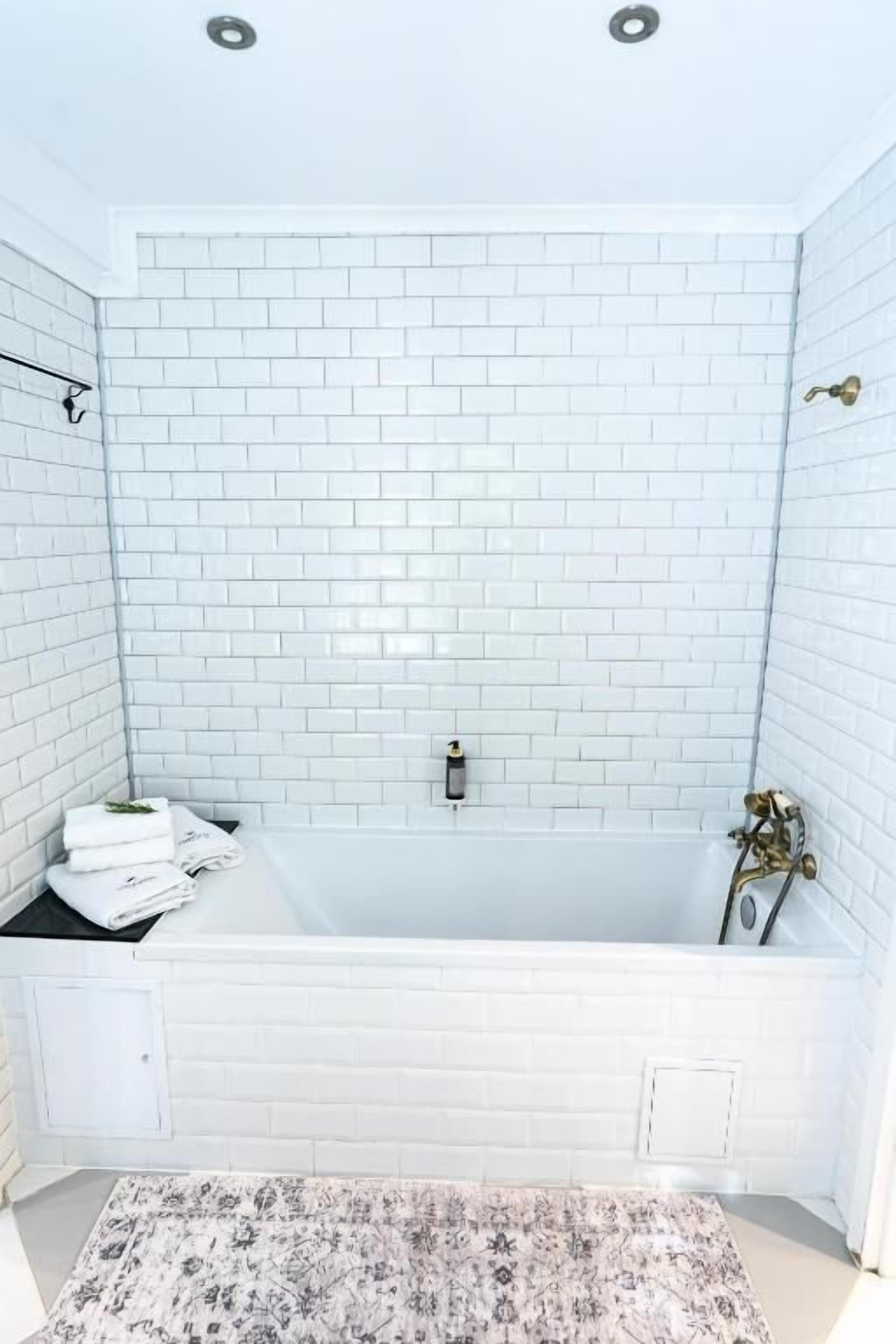 Ein Badezimmer mit weißen Fliesen, einer Badewanne und einer Duschkabine.