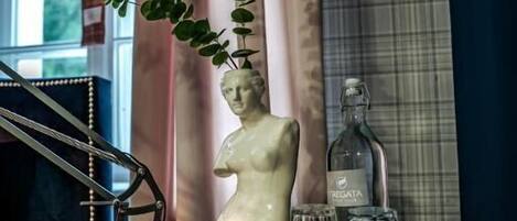 Un carrito bar con una escultura de busto blanco, una botella y vasos.