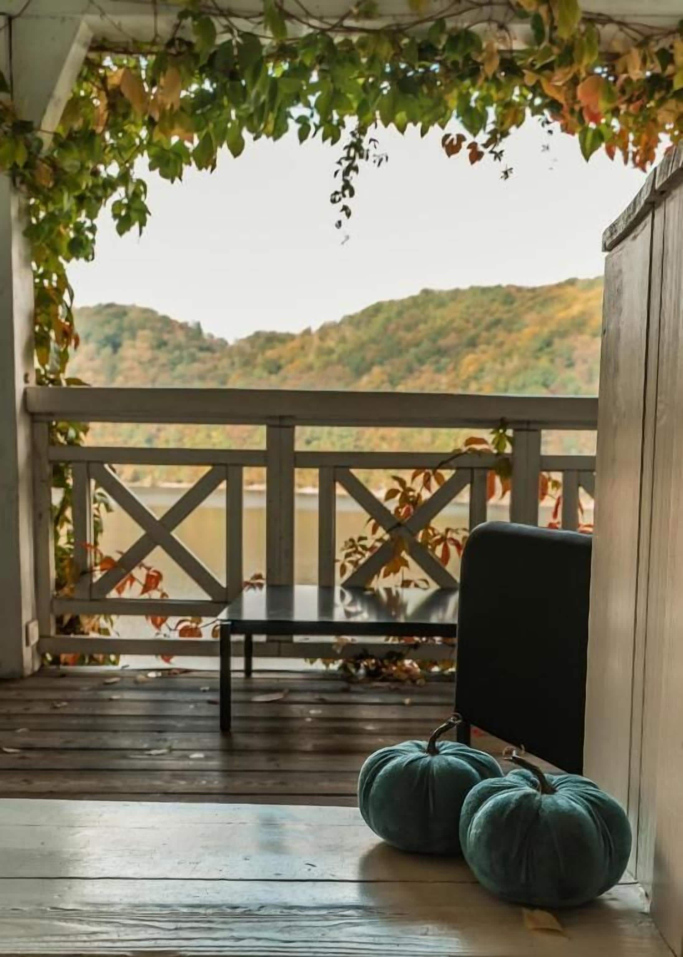 A porch with a bench, two pumpkins, and a view of a hilly landscape.