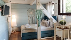 A bedroom with a bed, a hanging dreamcatcher, a lamp, and a window.