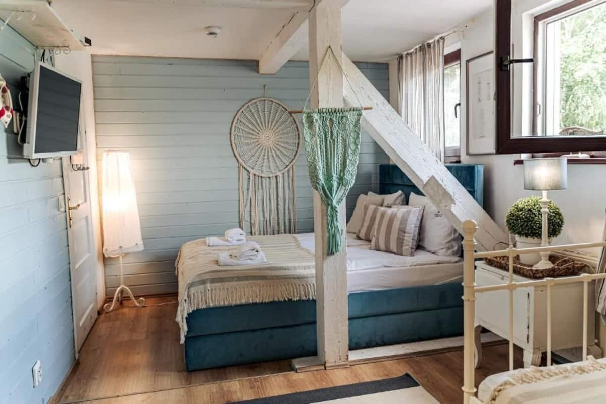 A bedroom with a bed, a hanging dreamcatcher, a lamp, and a window.