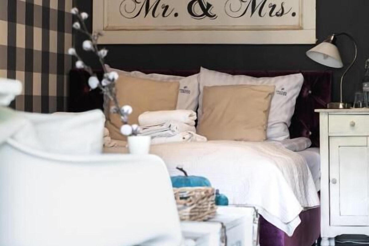 Un dormitorio con una cama, una mesita de noche, una lámpara y un cartel en la pared que dice 'Mr. & Mrs'.