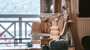 A cozy room with a wooden table, a vase with branches, and a sofa with a cushion.