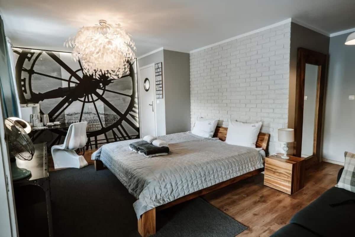 A bedroom with a bed, a desk, a chair, a large wall clock, and a unique wall decoration.
