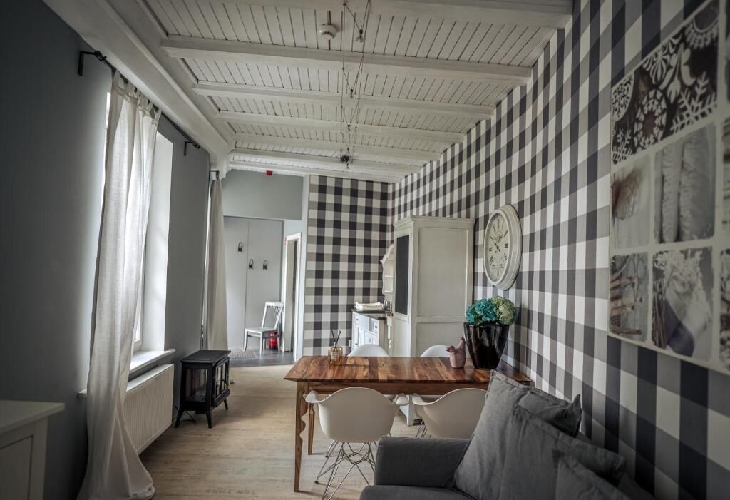 A dining area with a checkered wall, a wooden table, white chairs, and a clock.