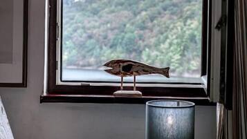 A window with a view of a forested hill, a lamp, and a small potted plant.