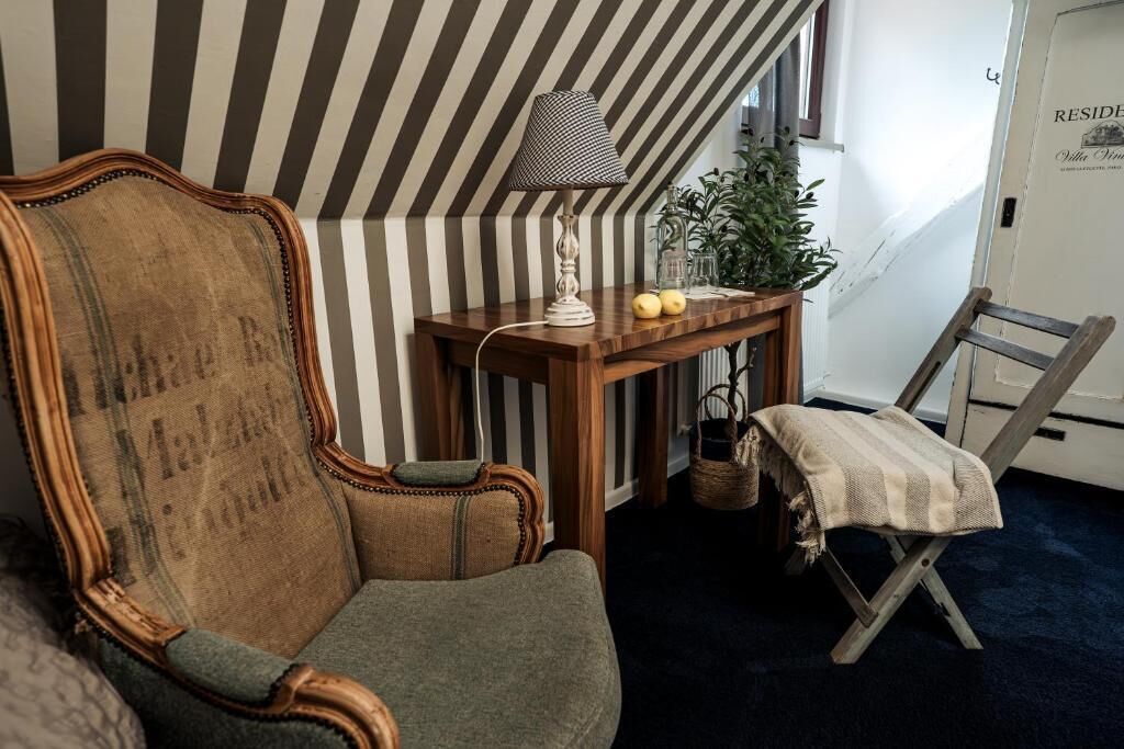 A room with a striped wall, a wooden chair, a small table with a lamp, a plant, and a ladder.