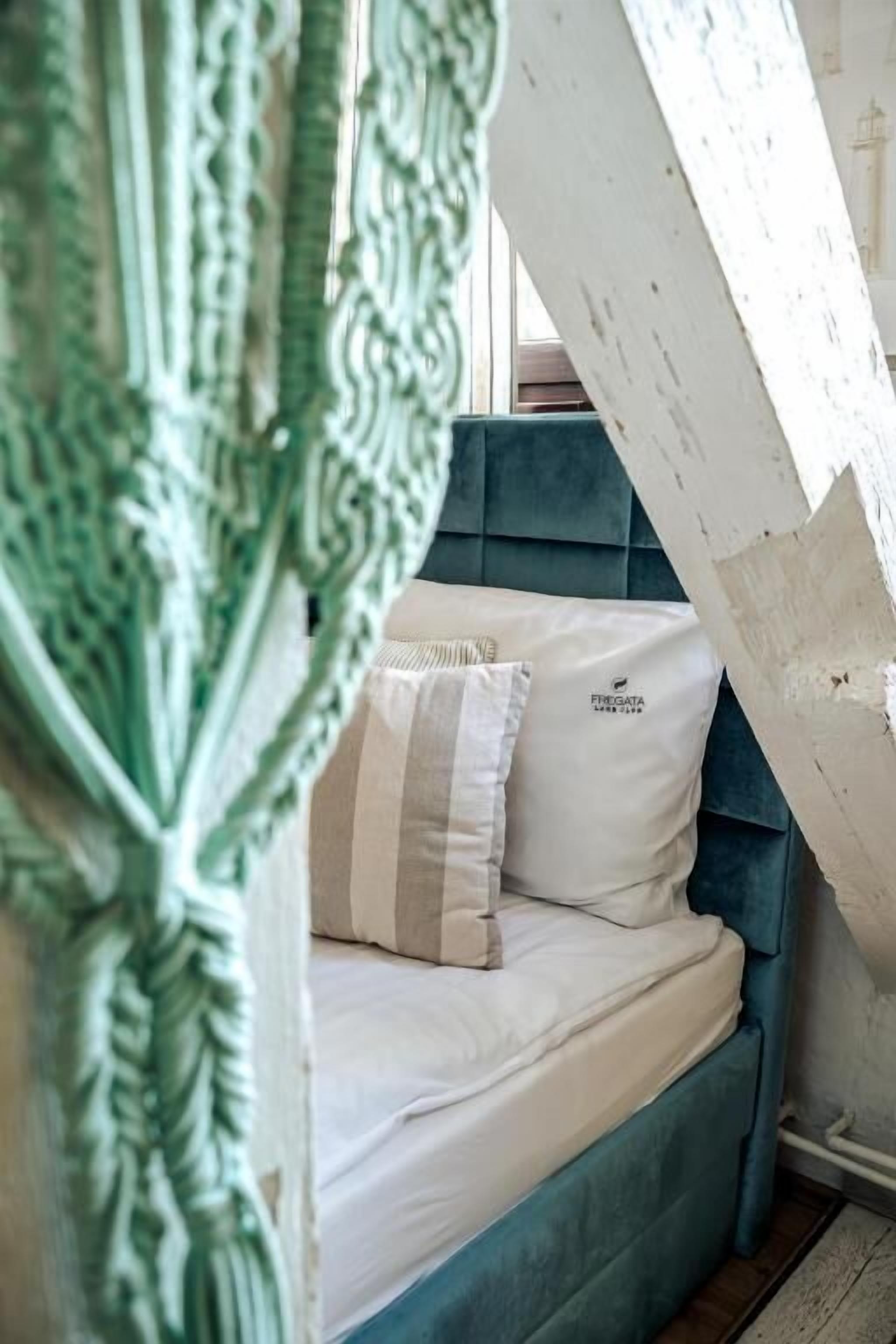 A bed with a white mattress and two pillows, a teal headboard, and a window with curtains.