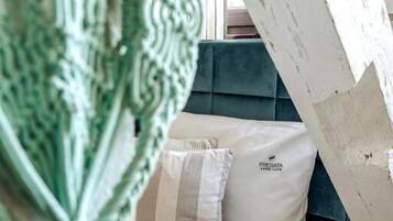 A bed with a white mattress and two pillows, a teal headboard, and a window with curtains.