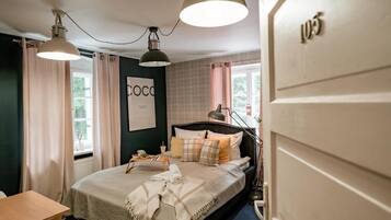 A bedroom with a bed, bedside table, lamp, curtains, and a window.