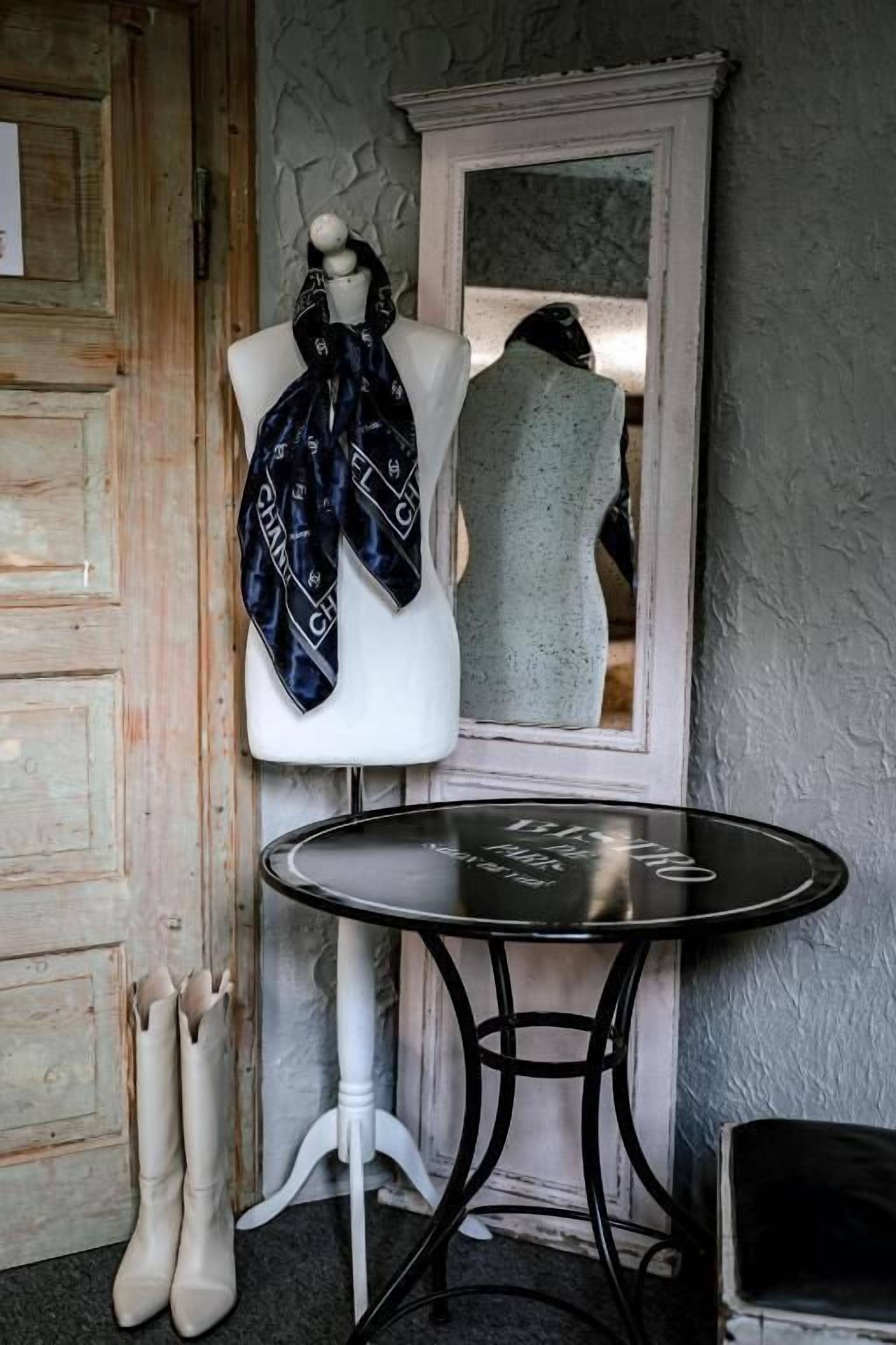 A mannequin with a scarf, a table, and a pair of boots.