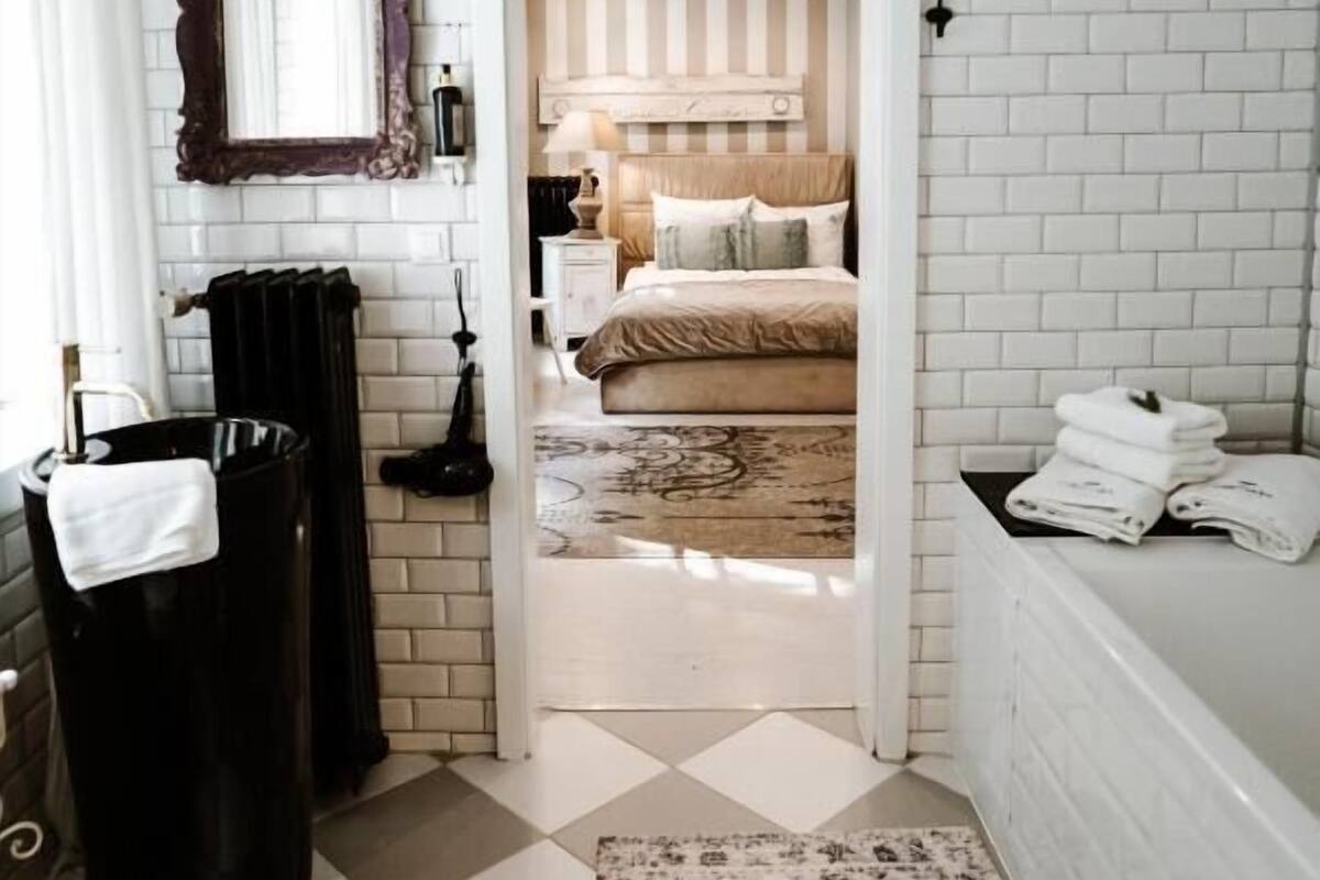 A bathroom with a white tiled wall, a black trash bin, a white toilet, and a patterned rug.
