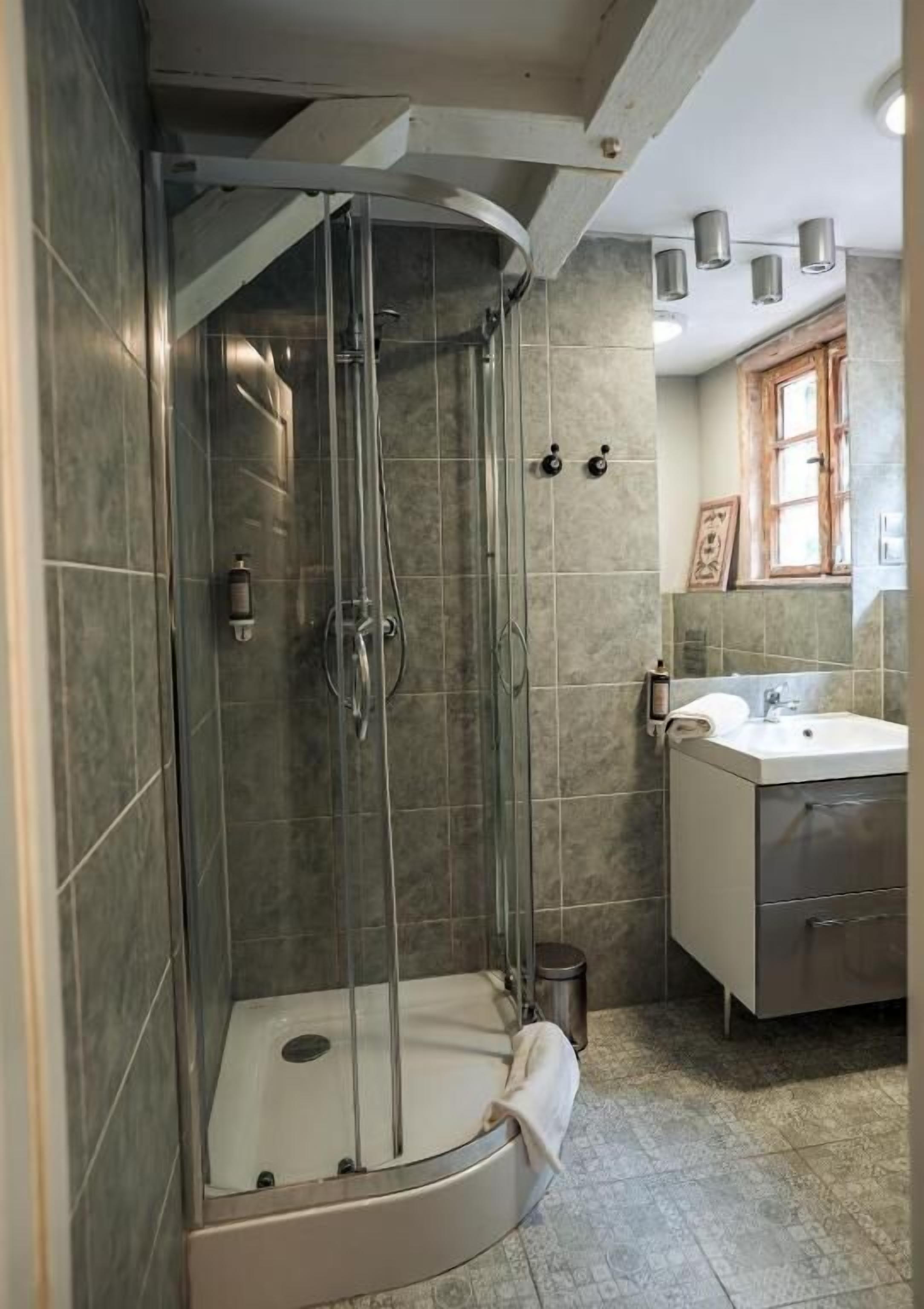 Ducha con puerta de vidrio, lavamanos y ventana con marco de madera.