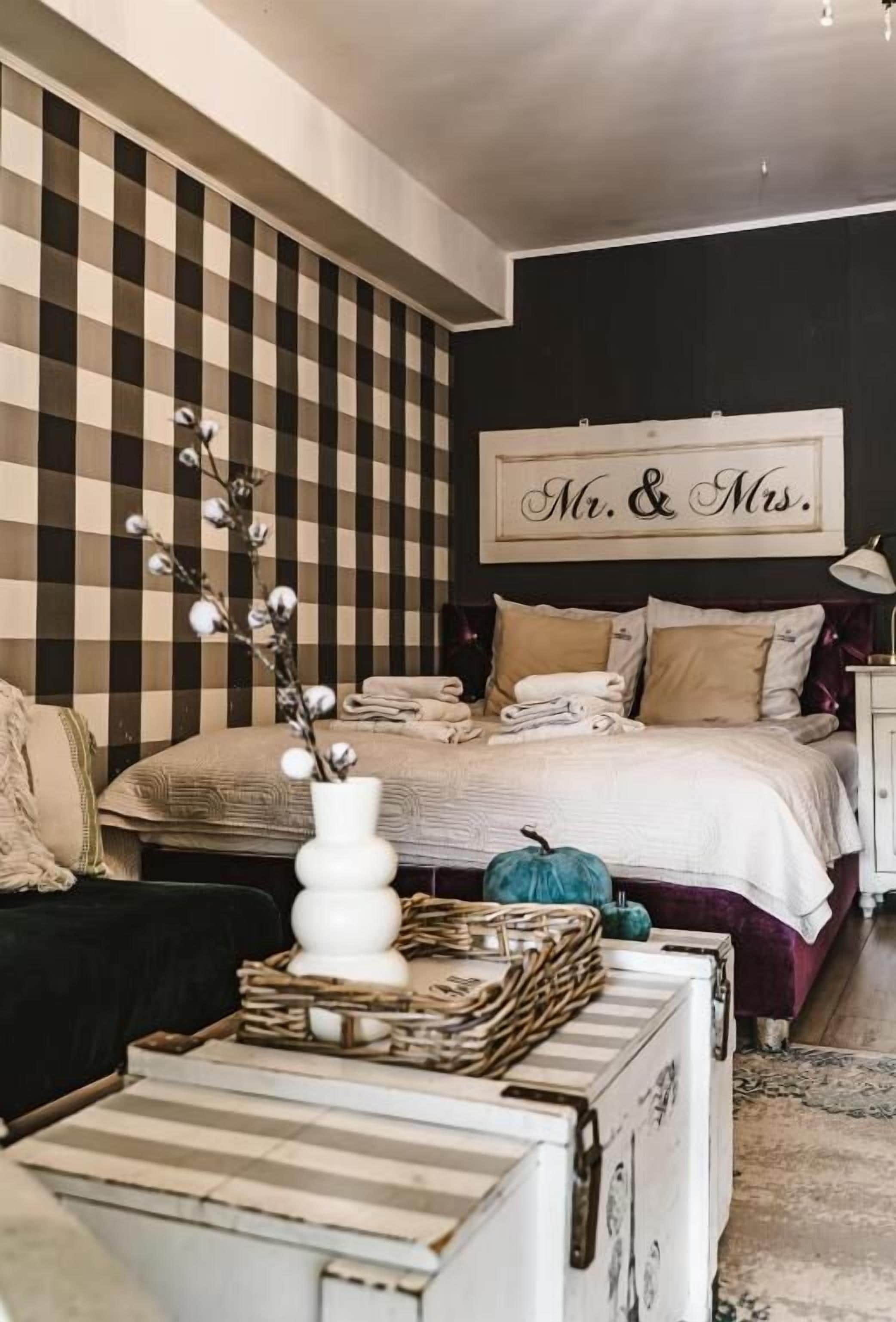 Un dormitorio con pared a cuadros, una cama con almohadas y un cartel que dice 'Mr. & Mrs.', además de un jarrón sobre una mesita de noche.