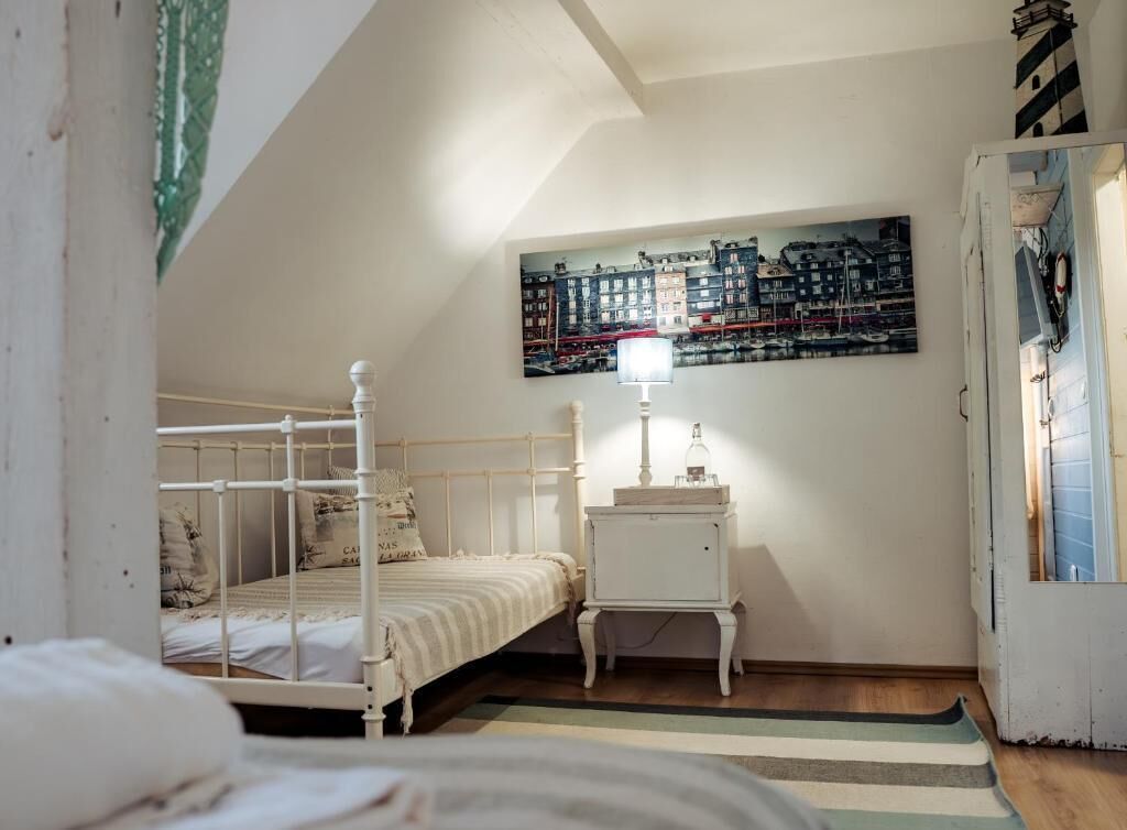 A bedroom with a bed, a nightstand, a lamp, a painting, and a door.