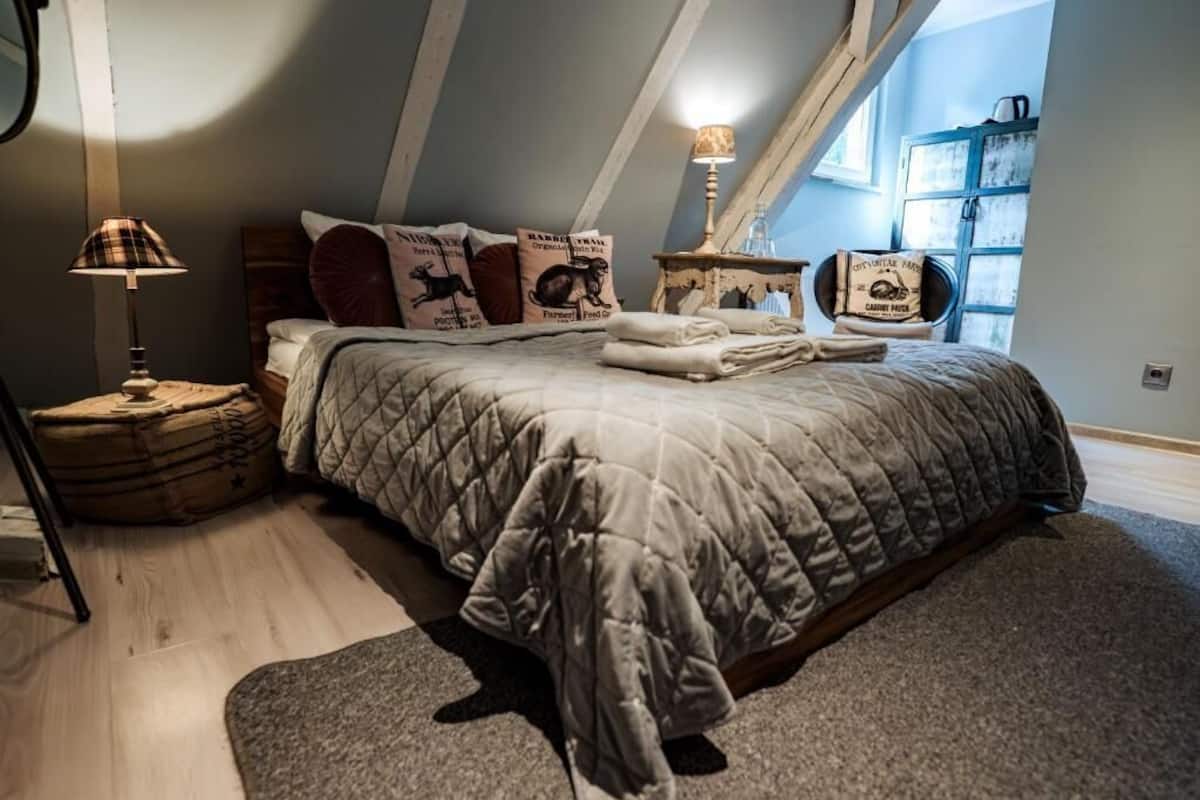 A bedroom with a large bed, a nightstand, a lamp, and a window with a view.