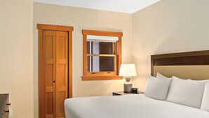 Ein Hotelzimmer mit einem Bett, einem Nachttisch mit Lampe, einem Holzschrank und einem Fenster mit Holzzarge.