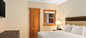 Ein Hotelzimmer mit einem Bett, einem Nachttisch mit Lampe, einem Holzschrank und einem Fenster mit Holzzarge.